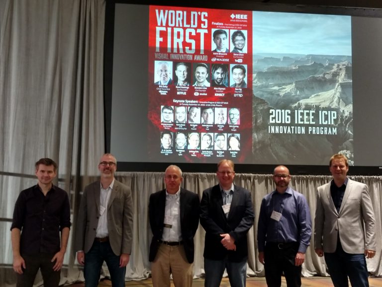 Six men designated as speakers for the 2016 IEEE Intl. Conference on Image processing are shown standing in front of a stage.