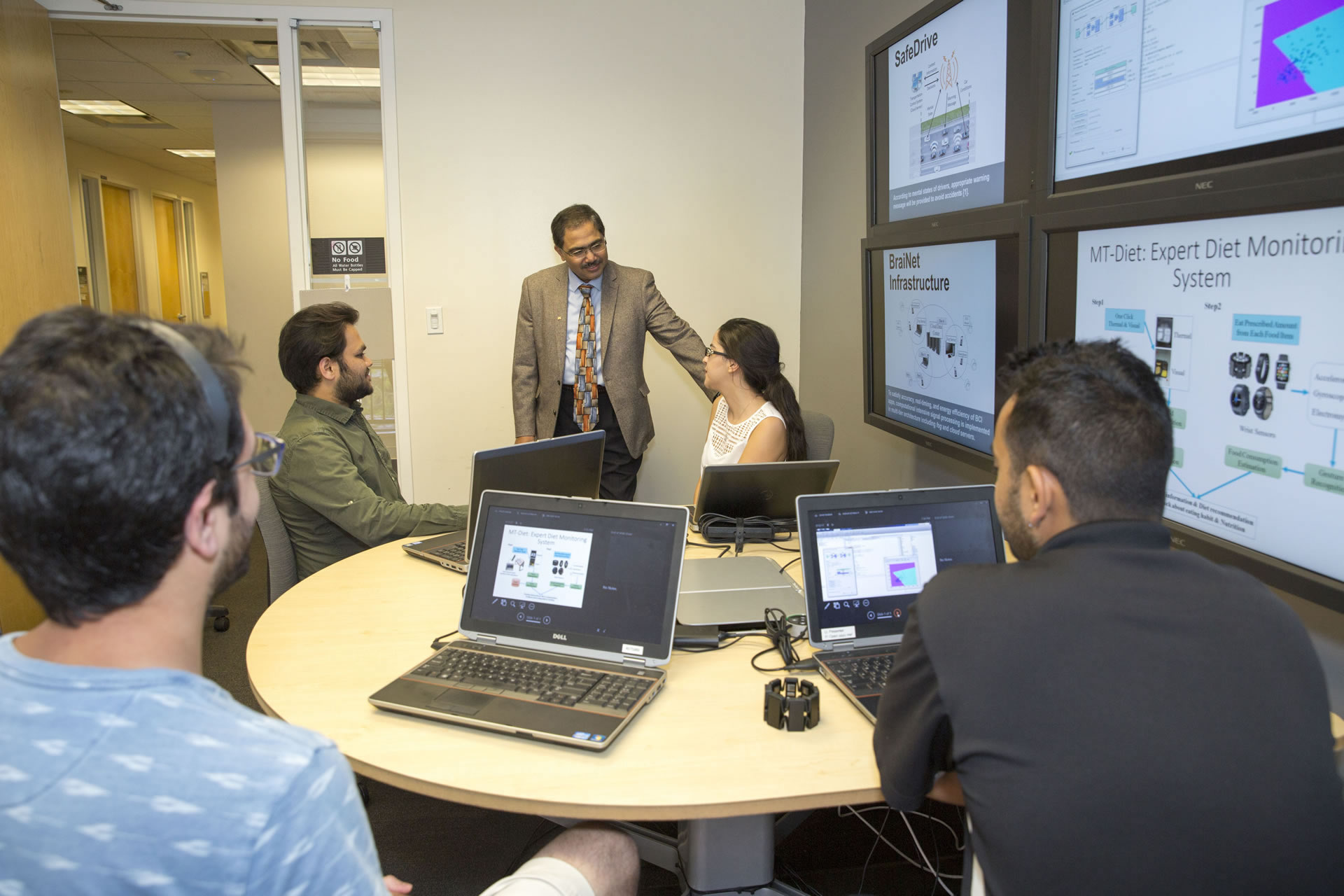 A faculty member talks with students in a computer lab