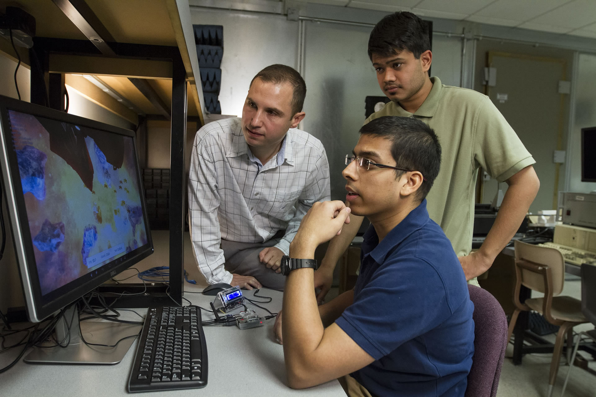 Students and a faculty member look at a program on a computer screen